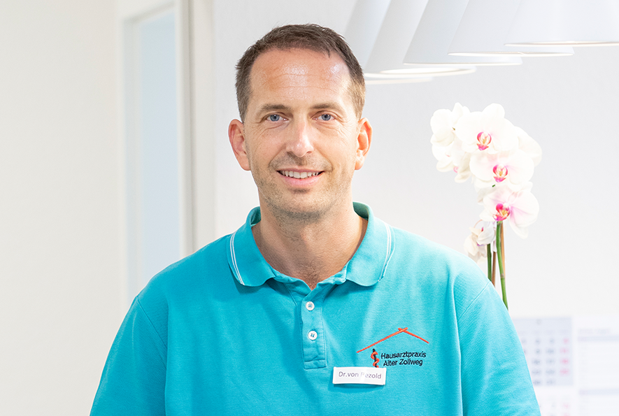 Das Foto ist eine Porträtaufnahme von Dr. Michael von Bezold. Er trägt ein T-Shirt mit dem Logo seiner Hausarztpraxis und lächelt in die Kamera.