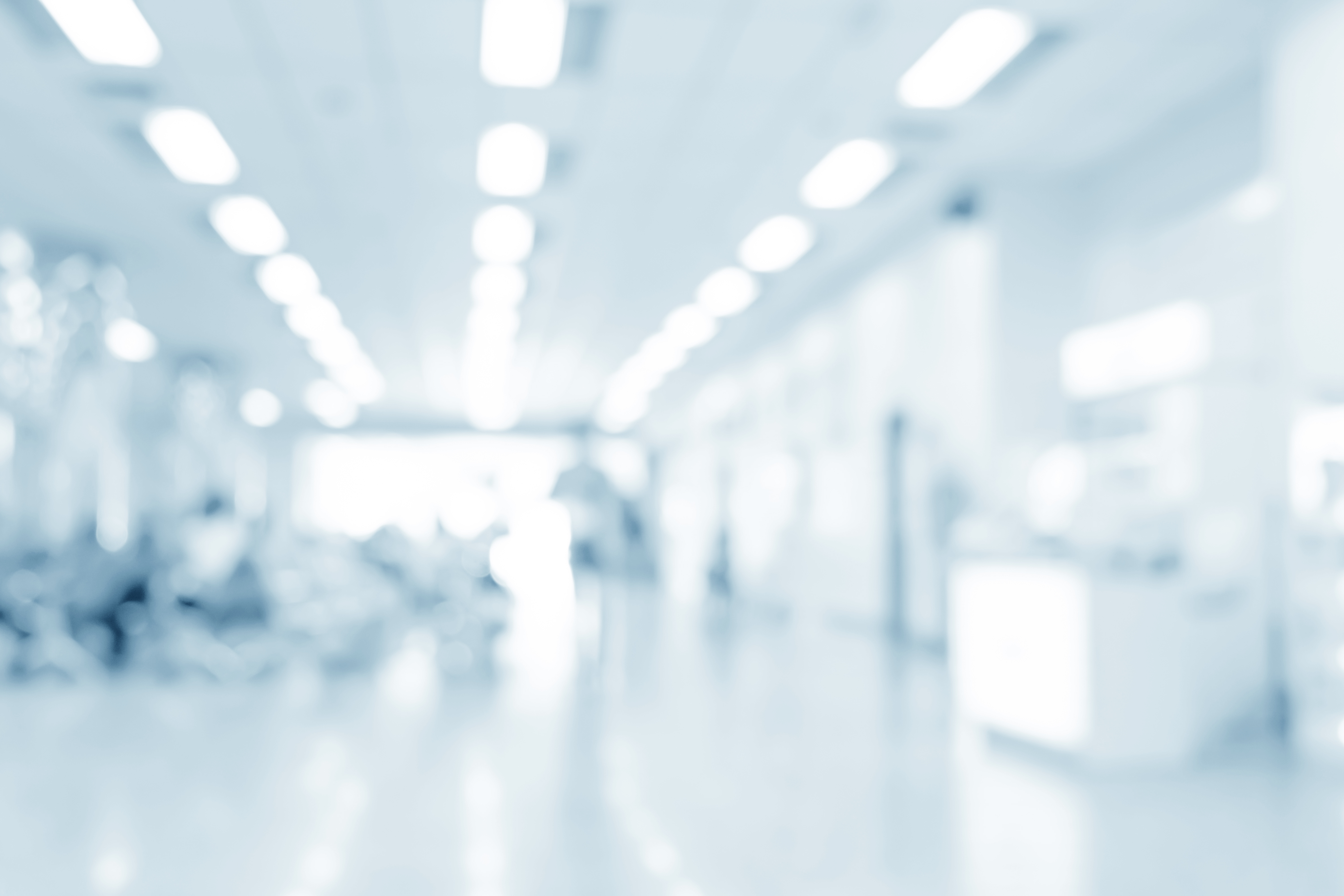 Zu sehen ist ein verschwommener Krankenhausflur. Das Licht ist sehr hell und grell.