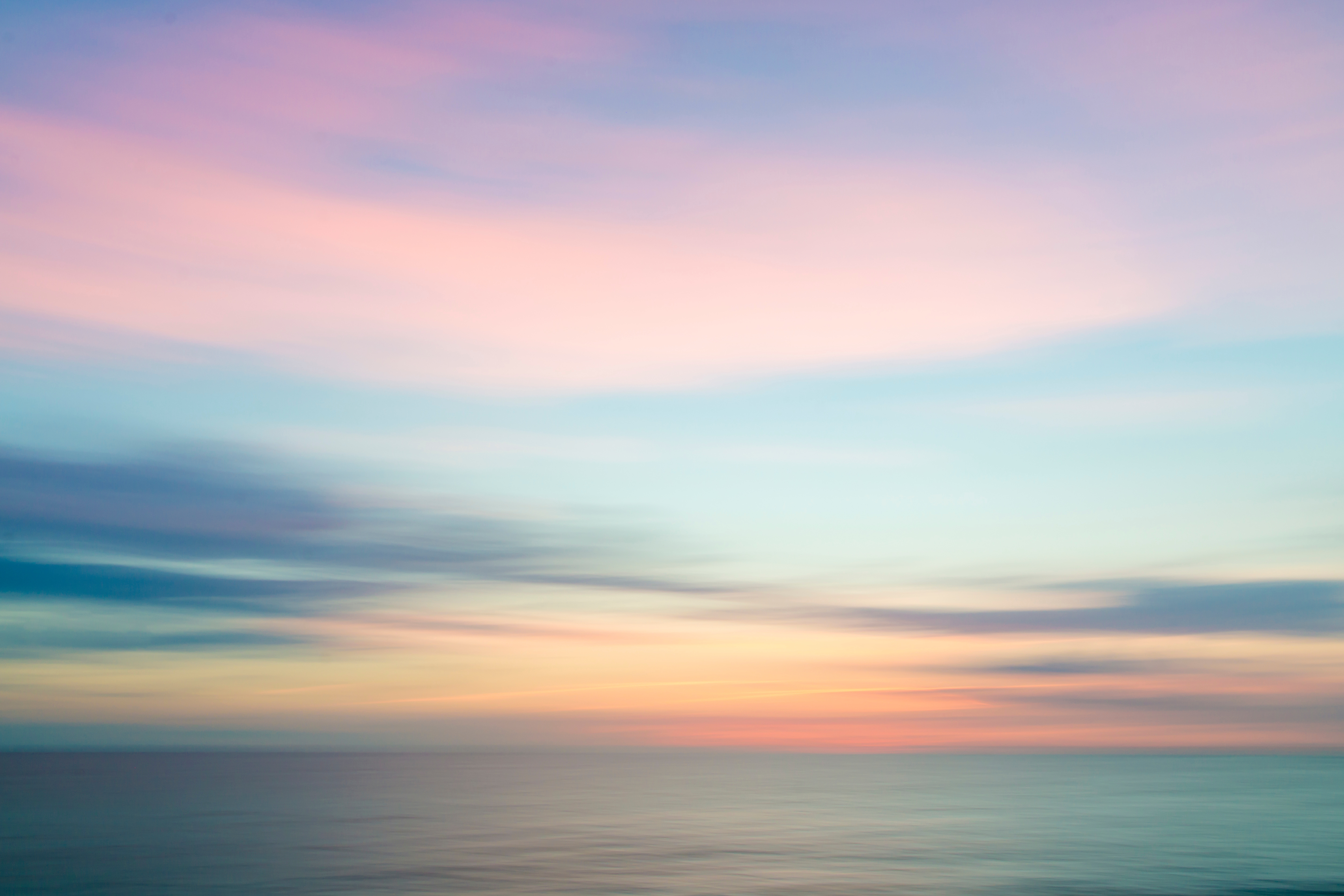 Zu sehen ist ein Horizont mit einer untergehenden Sonne samt Abendhimmel über einem ruhigen Meer.
