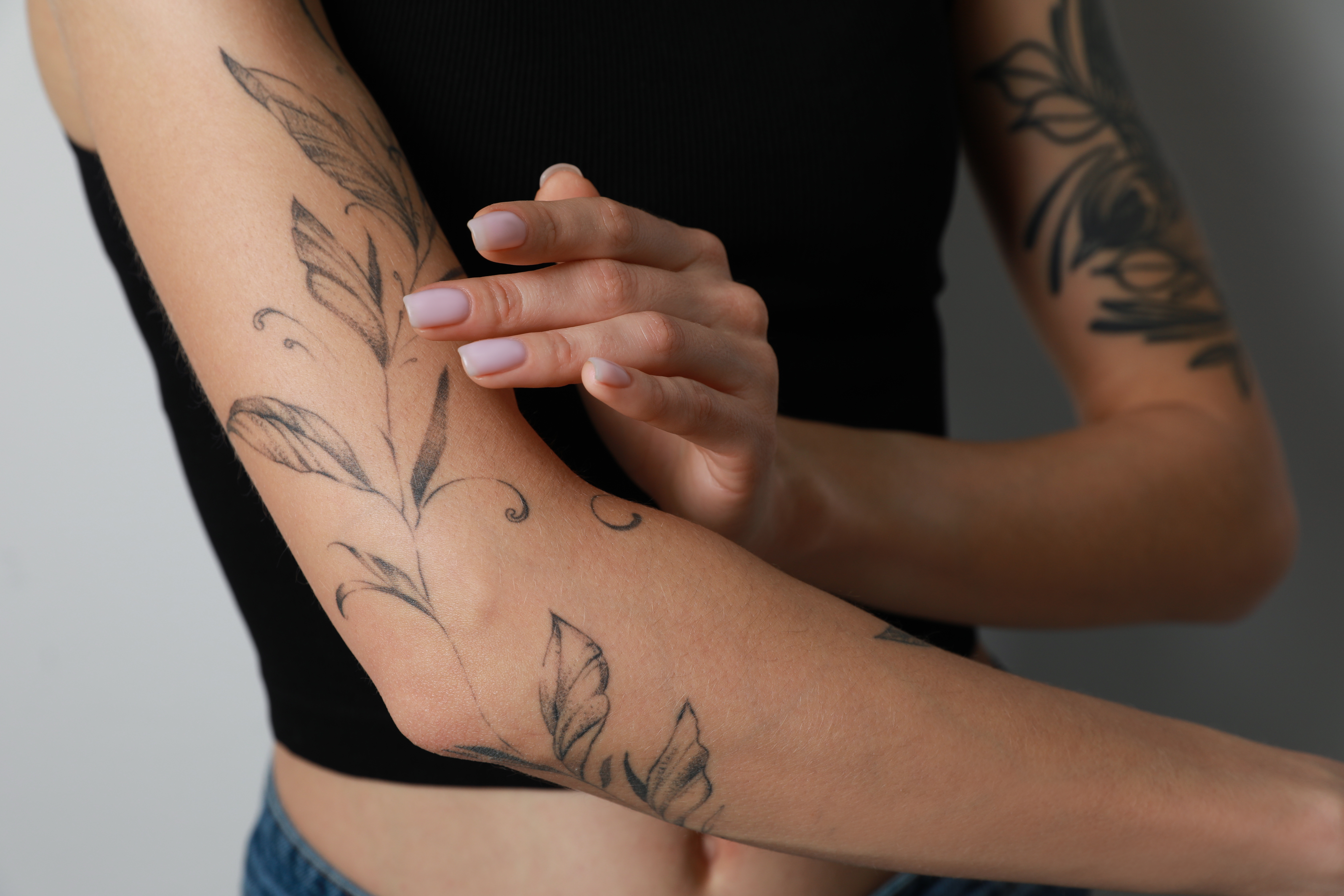 Eine Frau cremt ihr Tattoo auf dem Arm ein. Bei dem Tattoo handelt es sich um eine rankende Pflanze, die sich um den oberen Unterarm und den Oberarm schlängelt.