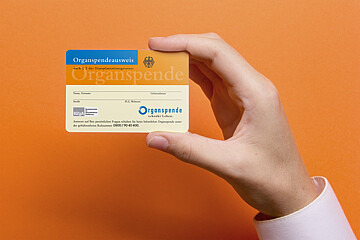 Das Foto zeigt einen Organspendeausweis, der von einer Hand in die Kamera gehalten wird. Der Hintergrund ist orange.