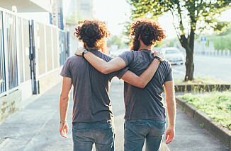 Zwei Männer, wahrscheinlich Zwillingsbrüder, laufen Arm in Arm eine Straße entlang.