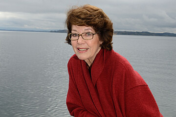 Dr. Marianne Koch lächelt in die Kamera. Sie lehnt an einem Steg. Im Hintergrund befindet sich ein See. 