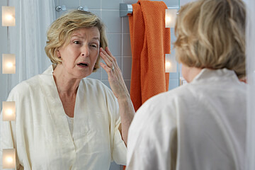 Fallbeispiel: Patientin Maria Dahl schaut in den Spiegel und stellt fest, dass ihr Augenlid etwas hängt.