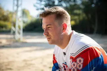 Herr Koch sitzt drau&szlig;en an einem Feldweg. Er ist von der Seite zu sehen und schaut nachdenklich in die Ferne.