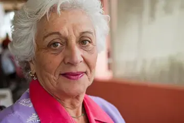 Zu sehen ist eine &auml;ltere Frau in Portraitansicht, die in die Kamera l&auml;chelt.