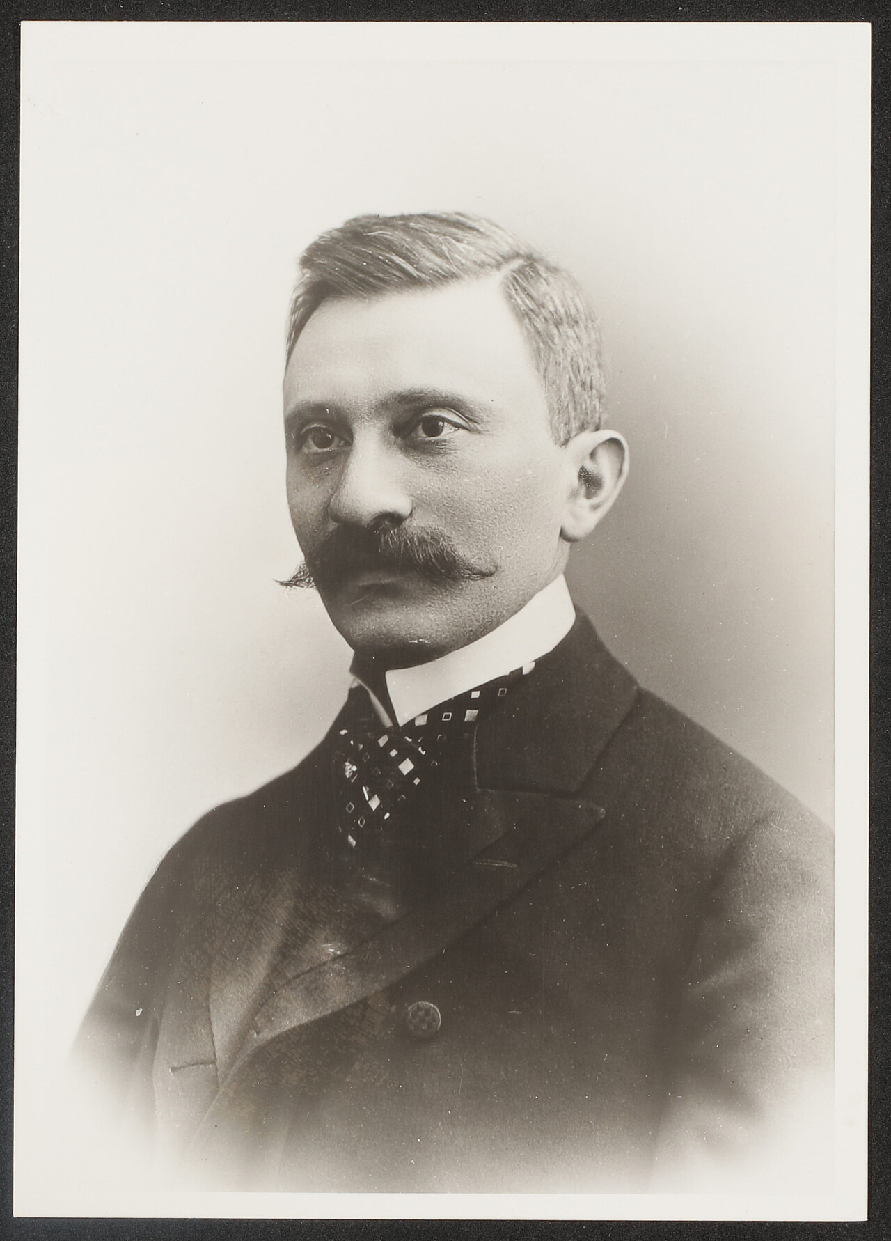 Die schwarz-weiß Aufnahme ist ein historisches Porträt des österreichischen Chirurgen Emmerich Ullmann. Er ist zur linken Seite gedreht und schaut an der Kamera vorbei. Er trägt einen geraden Scheitel, Schnäuzer und einen Anzug mit weißem Stehkragen.