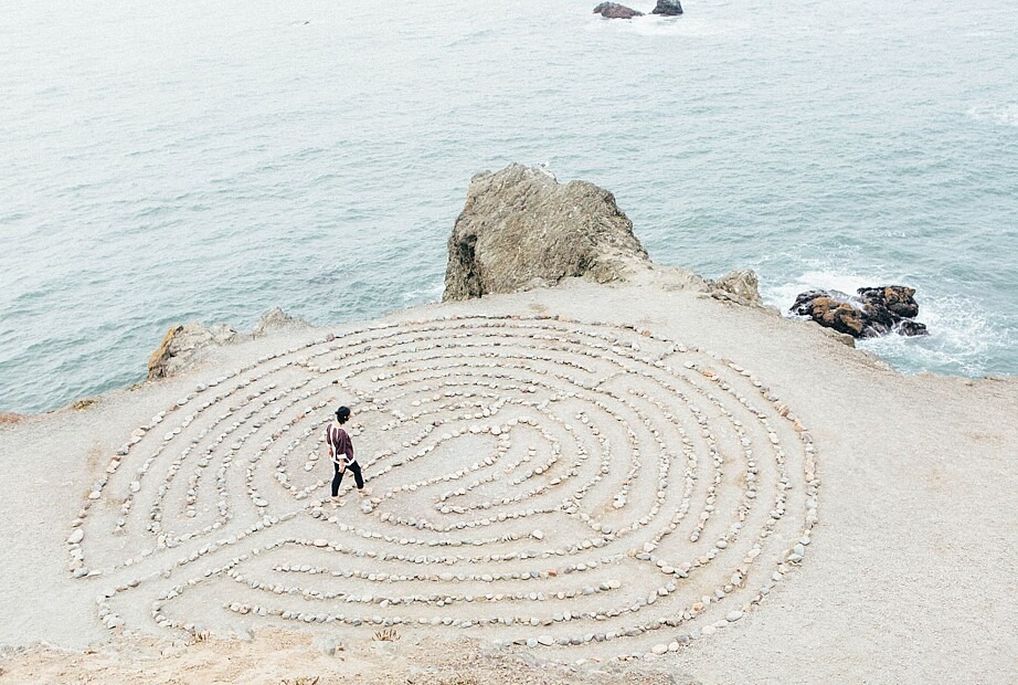 Eine Person läuft durch ein rundes Labyrinth aus Steinen direkt am Meer.