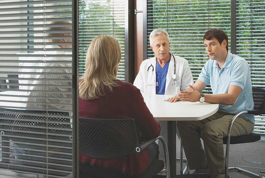 Das Foto zeigt ein Angehörigengespräch. Ein Arzt und ein Mitarbeiter der DSO sitzen einer Frau und einem Mann gegenüber. Der Mitarbeiter erklärt etwas und gestikuliert dabei.