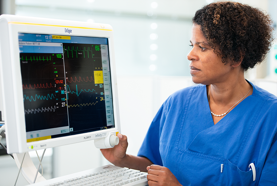 Dr. Geraldine de Heer steht neben einem EKG-Monitor. Sie schaut fokussiert auf den Bildschirm und hält eine Hand an den Monitor.