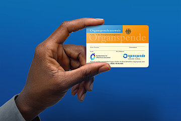 Ein Organspendeausweis wird von einer Hand hoch und frontal in die Kamera gehalten. Der Hintergrund ist blau.