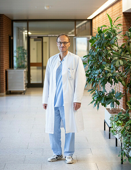 Dr. Frank Logemann steht in einem Krankenhausflur. Er trägt Krankenhauskleidung. 