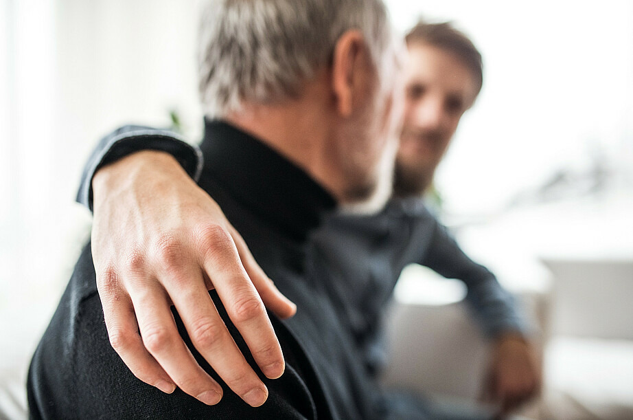 Zwei Männer sitzen auf einem Sofa und unterhalten sich. Beide sind nur verschwommen zu erkennen. Der Mann im Hintergrund legt den Arm um die Schultern des Mannes im Vordergrund.