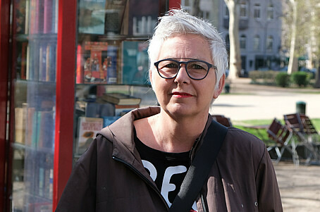 Die 55-jährige Ulla schaut direkt und freundlich in die Kamera. Sie hat graue kurze Haare und trägt eine Brille.