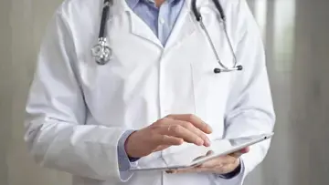 Zu sehen ist ein Arzt an einem Tablet, der eine Befragung ausf&uuml;llt.