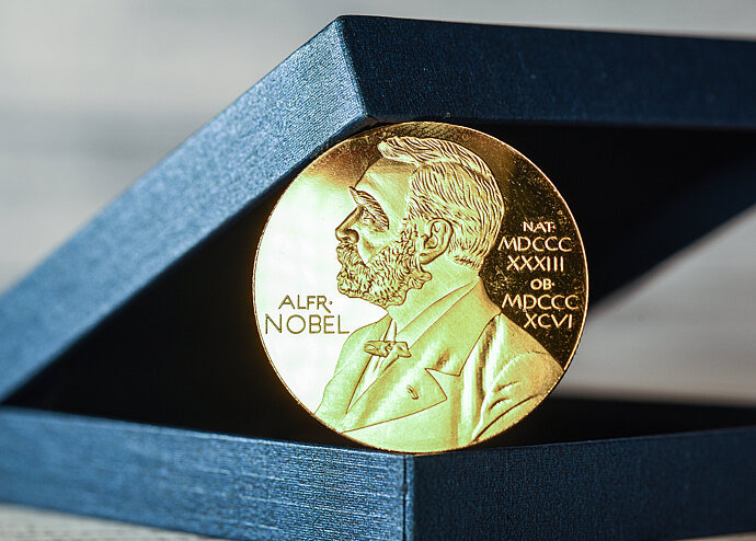 Das Bild zeigt eine Münze von Alfred Nobel mit einer Box.