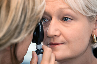 Eine Ärztin schaut einer Patientin mit einem speziellen Untersuchungsgerät ins Auge.