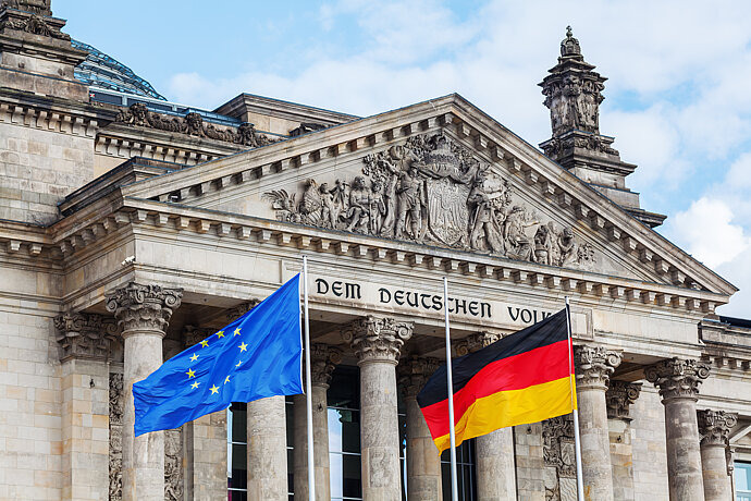 Das Bild zeigt den Bundestag in Berlin mit der Deutschen Flagge und der Europäischen Flagge.