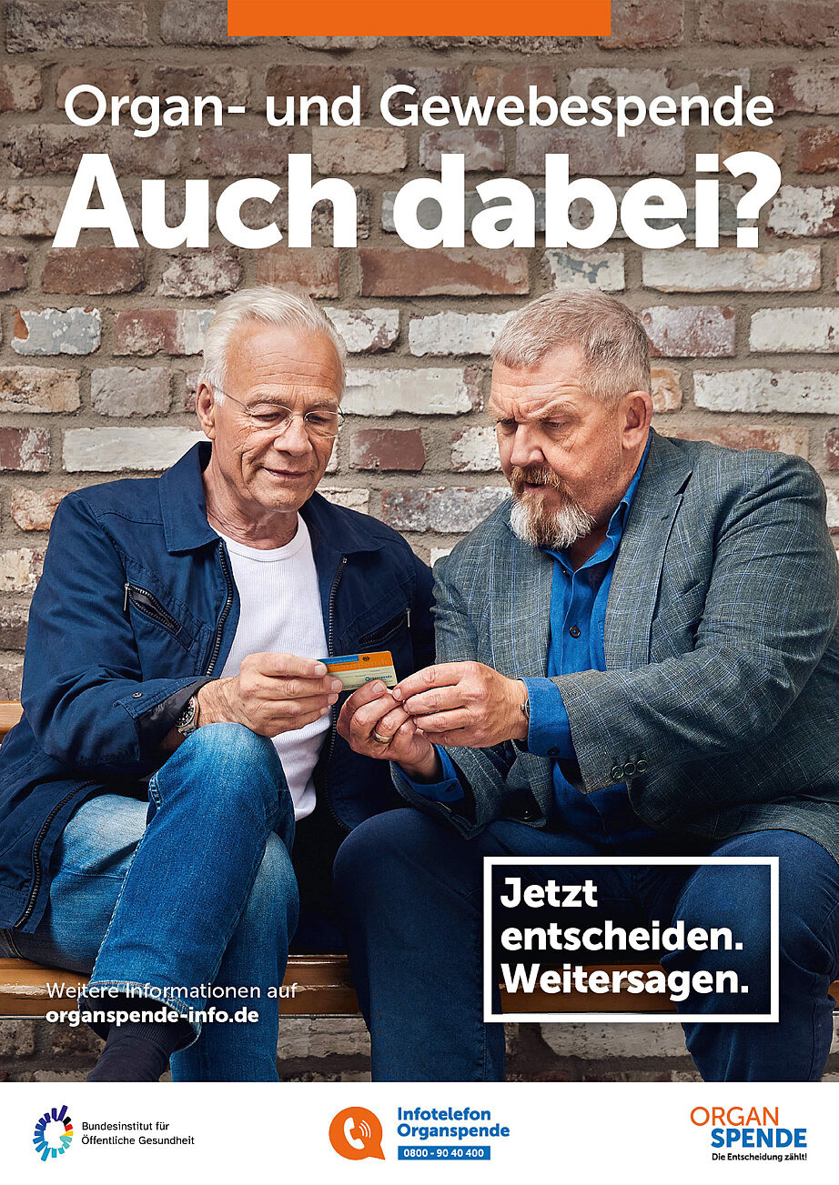Auf dem Plakat sind die beiden Schauspieler Dietmar Bär und Klaus J. Behrendt Plakat zu sehen. Sie sitzen nebeneinander und schauen auf einen Organspendeausweis, den sie in den Händen halten. Darüber stehen die Texte „Organ- und Gewebespende. Auch dabei?“ und „Jetzt entscheiden. Weitersagen.“