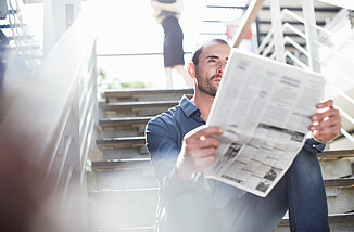 Ein Mann sitzt auf einer Treppe und liest Zeitung.