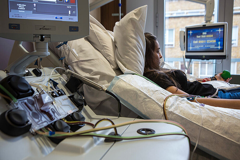 Zu sehen ist eine junge Frau, die im Bett liegt, w&auml;hrend eine Stammzellenspende durchgef&uuml;hrt wird.