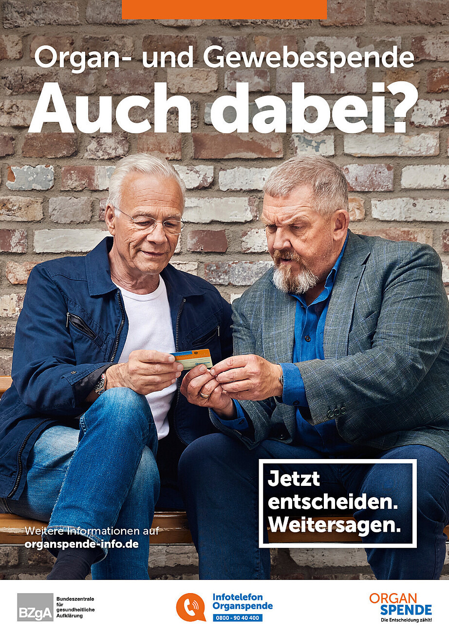 Auf dem Plakat sind die beiden Schauspieler Dietmar Bär und Klaus J. Behrendt Plakat zu sehen. Sie sitzen nebeneinander und schauen auf einen Organspendeausweis, den sie in den Händen halten. Darüber stehen die Texte „Organ- und Gewebespende. Auch dabei?“ und „Jetzt entscheiden. Weitersagen.“