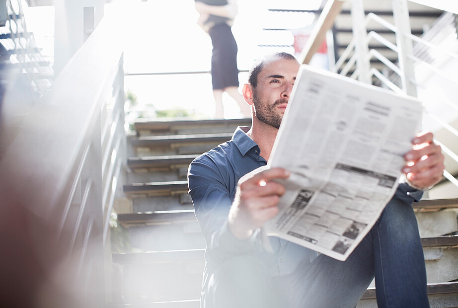 Ein Mann sitzt auf den Stufen einer Treppe und liest aufmerksam eine Zeitung.
