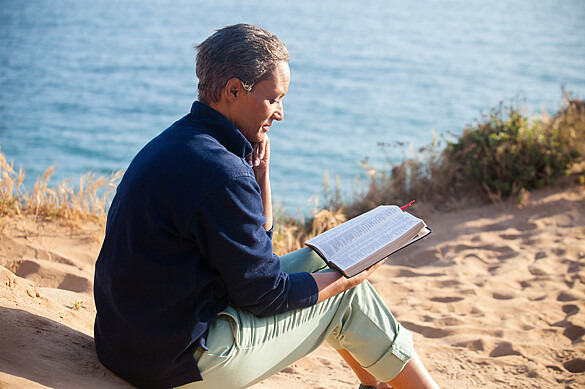 Eine junge Frau sitzt am Strand und liest in der Bibel. 
