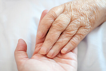 Die Hand eines älteren Menschen liegt in der Hand eines jüngeren Menschen.