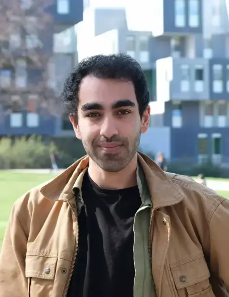 Der 30-j&auml;hrige Saed steht drau&szlig;en vor einer Wiese und blickt nach vorne freundlich in die Kamera. Er hat dunkle kurze Haare und tr&auml;gt ein dunkles Shirt und dar&uuml;ber eine braune Jacke..