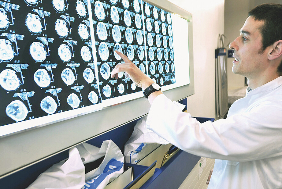Ein Arzt zeigt etwas auf einem Bildschirm, auf dem mehrere MRT-Aufnahmen eines Gehirns zu sehen sind.
