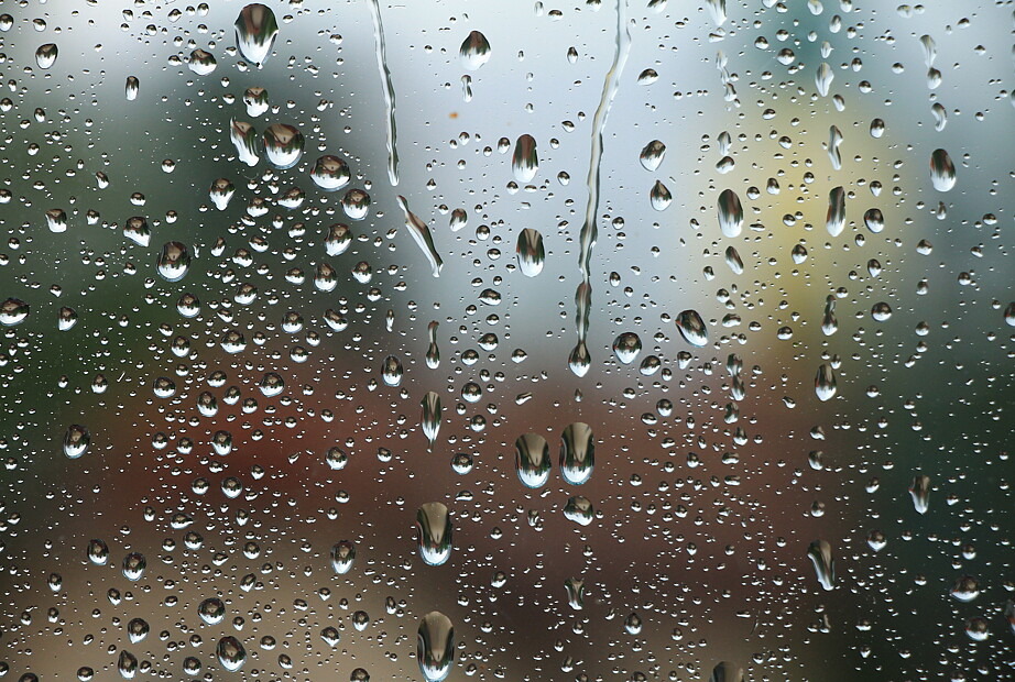Zu sehen ist eine Nahaufnahme von Regentropfen an einer Glasscheibe. Der Hintergrund ist verschwommen.